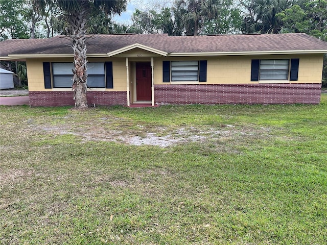 single story home with a shingled roof, a front yard, and concrete block siding