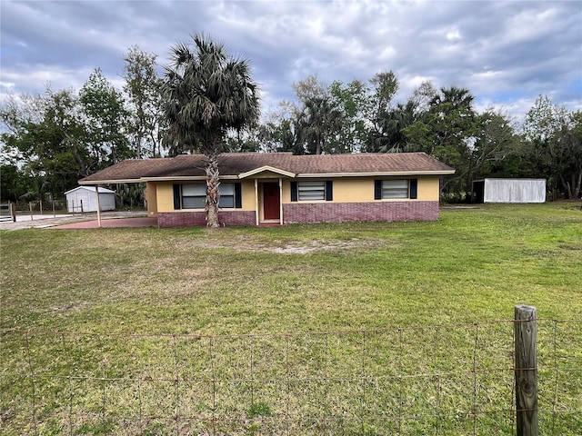 ranch-style house with an attached carport, an outbuilding, fence, a front yard, and brick siding