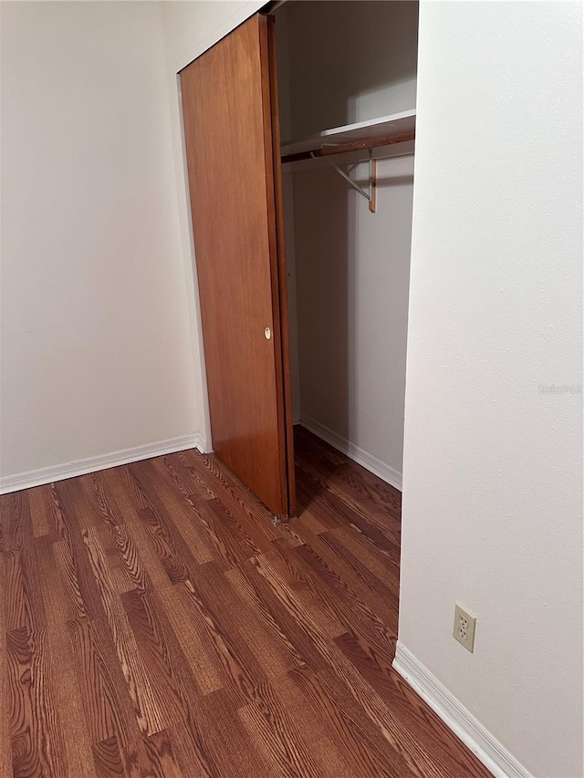 unfurnished bedroom with a closet, baseboards, and dark wood-type flooring