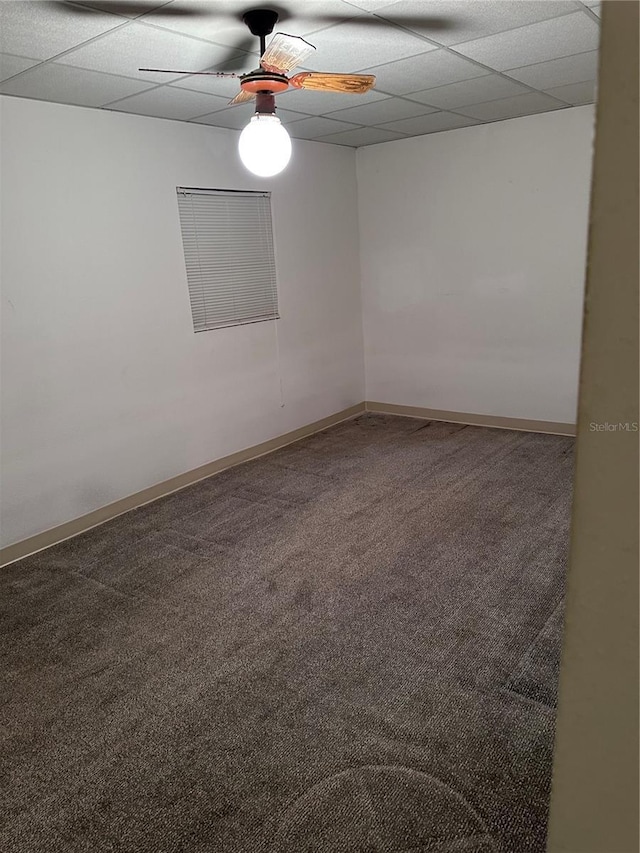 carpeted empty room featuring ceiling fan, a drop ceiling, and baseboards