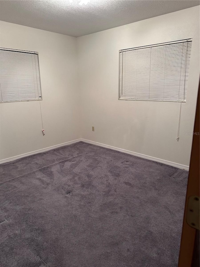 empty room featuring dark colored carpet, a textured ceiling, and baseboards