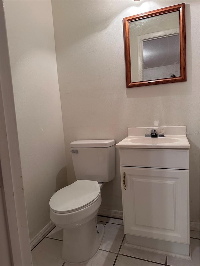 half bathroom featuring toilet, tile patterned flooring, baseboards, and vanity