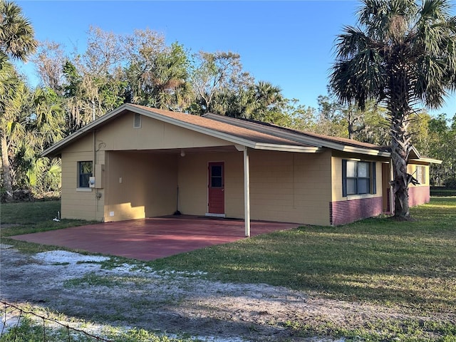 view of front of house featuring driveway, concrete block siding, an attached carport, and a front yard