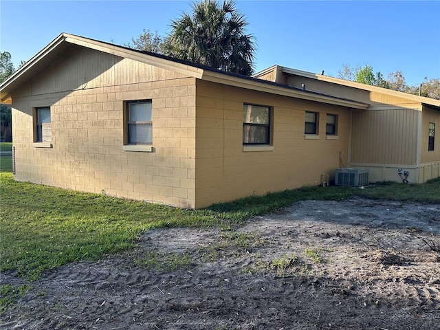 view of property exterior with central AC, a yard, and concrete block siding