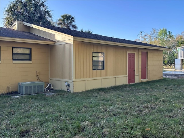 back of property featuring roof with shingles, central AC, and a yard