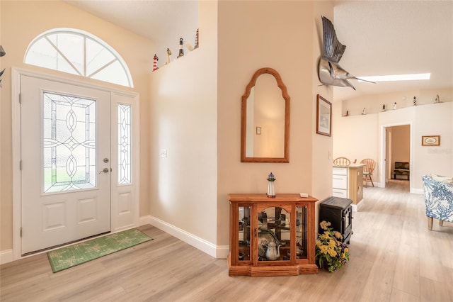 foyer featuring light wood finished floors, baseboards, and vaulted ceiling