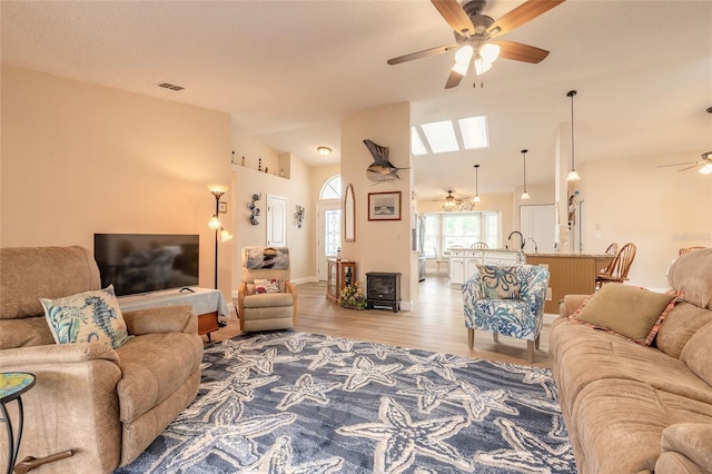 living area featuring vaulted ceiling, visible vents, light wood finished floors, and ceiling fan