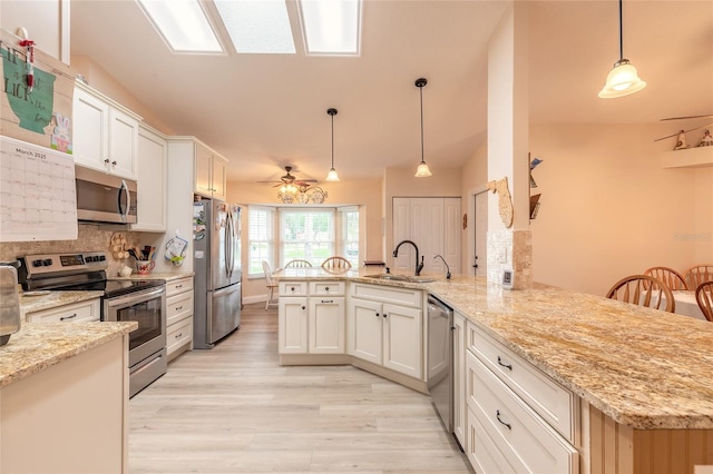 kitchen with a peninsula, a sink, stainless steel appliances, light wood-style floors, and white cabinetry