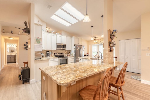 kitchen with visible vents, a sink, a kitchen breakfast bar, stainless steel appliances, and vaulted ceiling with skylight