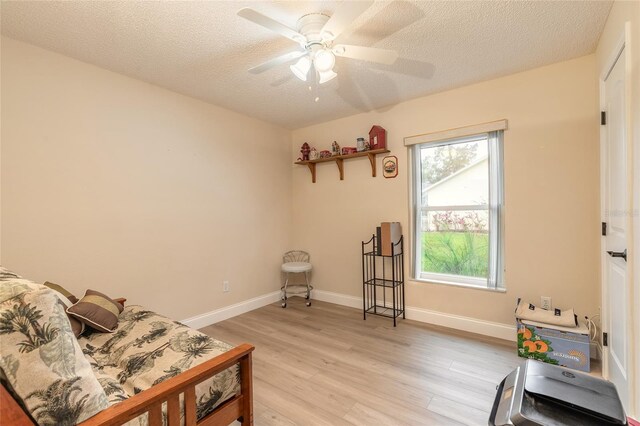 living area featuring baseboards, a textured ceiling, a ceiling fan, and light wood finished floors