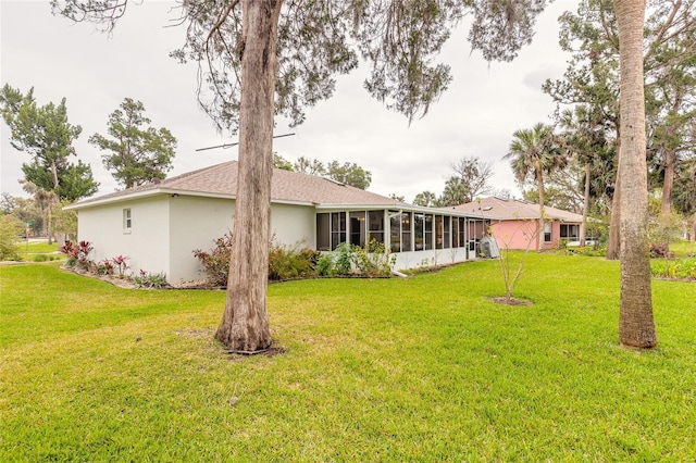 rear view of property with stucco siding, a lawn, and a sunroom