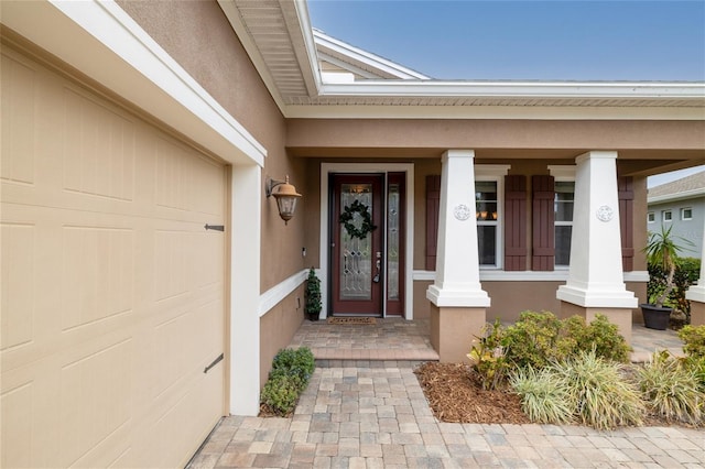 doorway to property with covered porch, an attached garage, and stucco siding