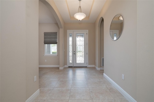 foyer featuring arched walkways, a raised ceiling, baseboards, and light tile patterned floors