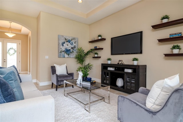 tiled living area with arched walkways, a raised ceiling, baseboards, and recessed lighting