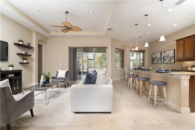 living area featuring baseboards, a tray ceiling, visible vents, and recessed lighting