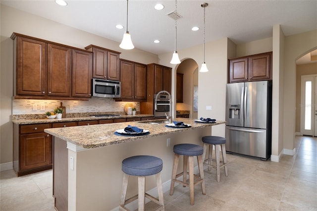 kitchen featuring light stone countertops, appliances with stainless steel finishes, arched walkways, and backsplash