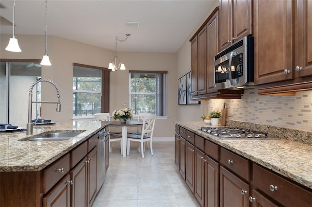 kitchen with tasteful backsplash, decorative light fixtures, light stone countertops, stainless steel appliances, and a sink