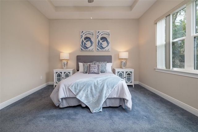 bedroom featuring a tray ceiling, dark carpet, and baseboards