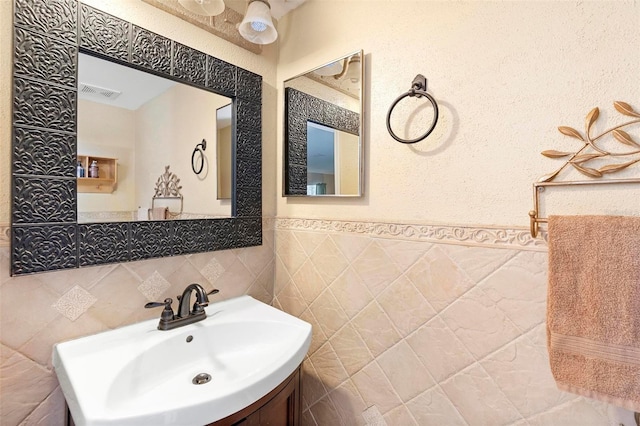 bathroom with visible vents, a wainscoted wall, vanity, and tile walls