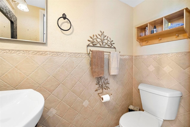 half bathroom with wainscoting, a sink, tile walls, and toilet