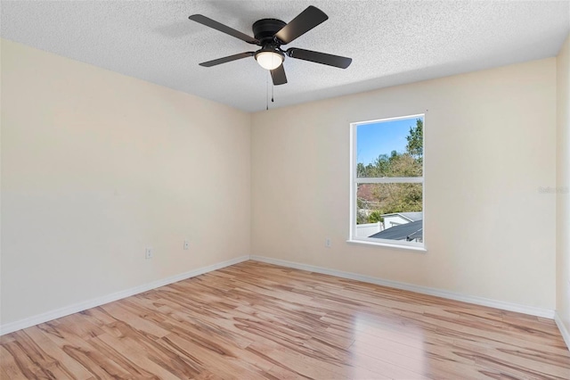 spare room featuring a textured ceiling, light wood-type flooring, a ceiling fan, and baseboards