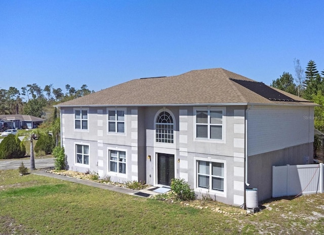 view of front facade featuring a front yard, fence, roof with shingles, and stucco siding