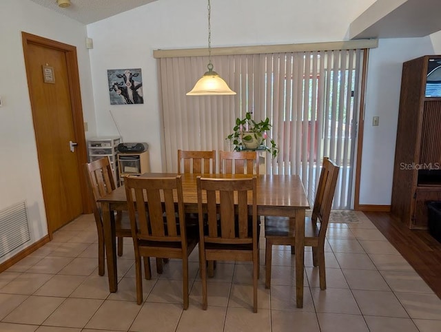 dining area featuring light tile patterned floors, vaulted ceiling, visible vents, and baseboards