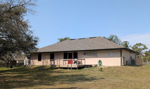 rear view of property featuring roof with shingles, a lawn, and fence