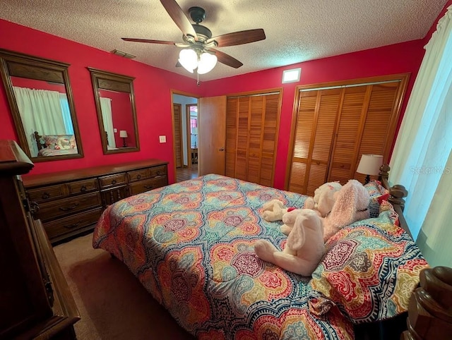 bedroom featuring a textured ceiling, ceiling fan, two closets, and visible vents