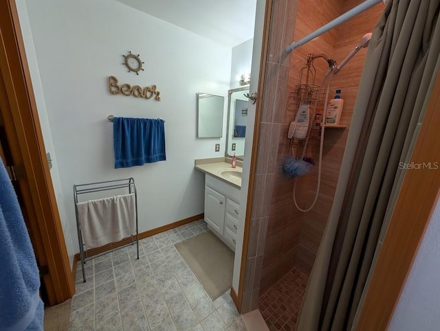 bathroom with baseboards, a tile shower, and vanity