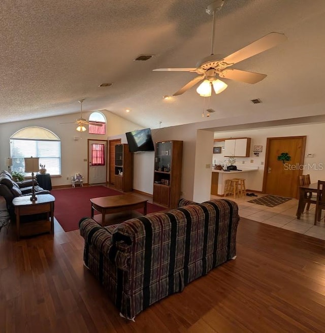 living area featuring lofted ceiling, visible vents, a textured ceiling, and wood finished floors