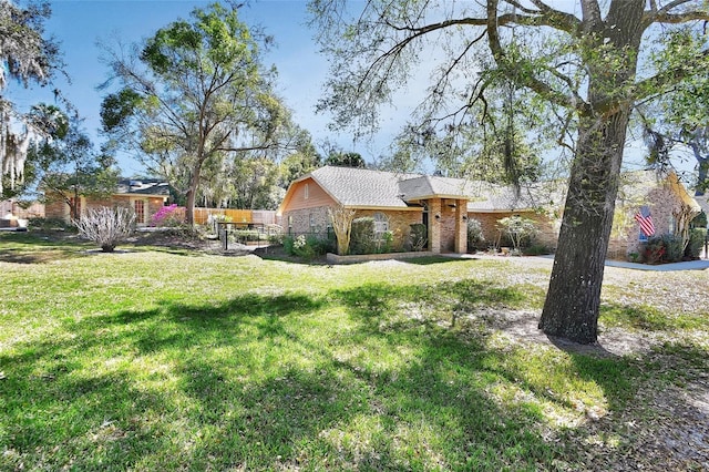 view of front of home featuring brick siding, fence, and a front lawn