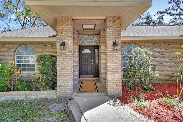 doorway to property featuring brick siding and roof with shingles