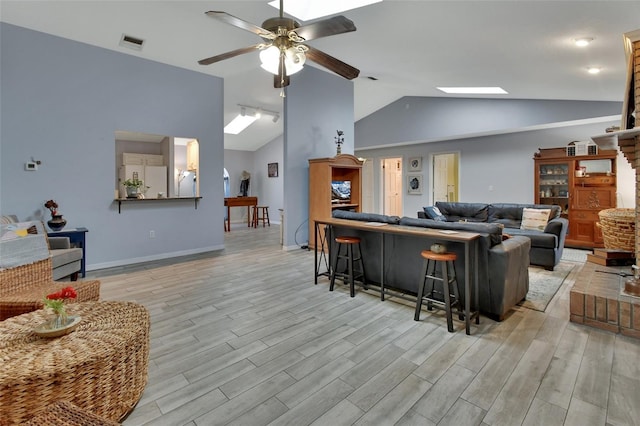 living area featuring light wood finished floors, visible vents, baseboards, lofted ceiling with skylight, and ceiling fan