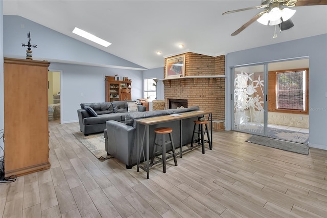 living room featuring light wood-style floors, vaulted ceiling with skylight, baseboards, and a ceiling fan