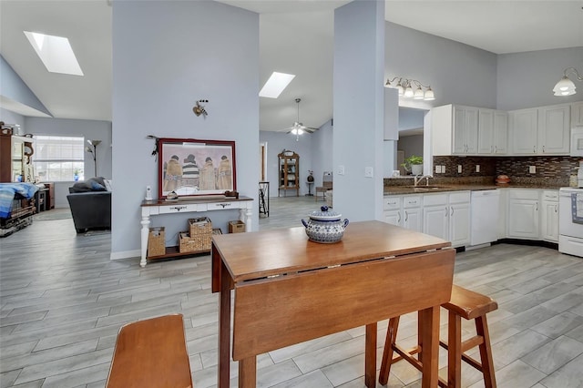 kitchen featuring a skylight, tasteful backsplash, white cabinetry, a sink, and white appliances