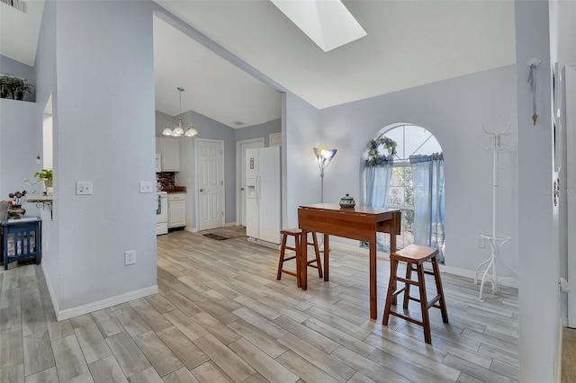 interior space with light wood finished floors, visible vents, a chandelier, vaulted ceiling with skylight, and baseboards