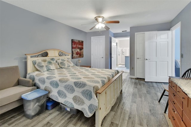 bedroom with ceiling fan, visible vents, baseboards, multiple closets, and light wood finished floors