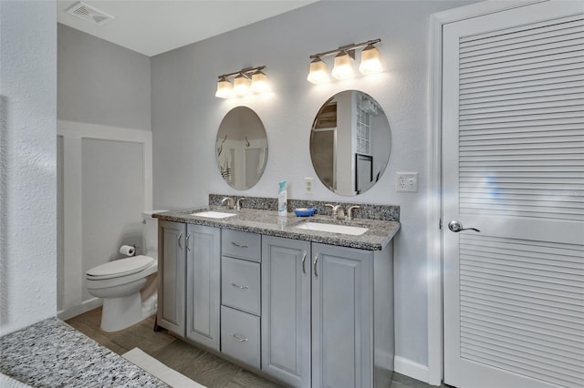 bathroom featuring toilet, double vanity, a sink, and visible vents