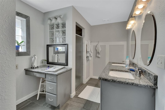 bathroom with double vanity, a stall shower, a sink, and baseboards