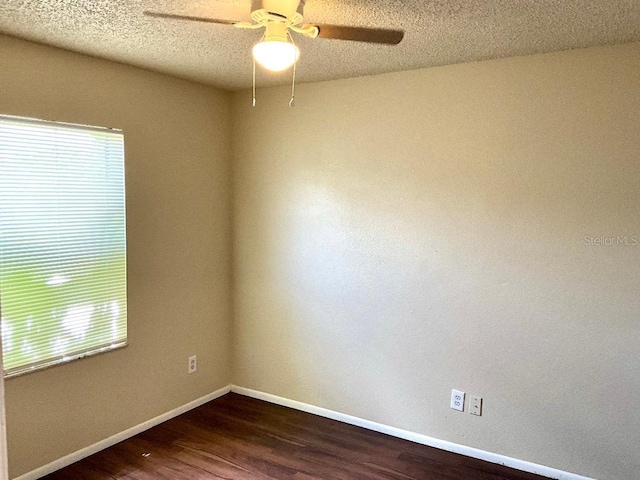 empty room featuring dark wood-style floors, baseboards, a ceiling fan, and a healthy amount of sunlight