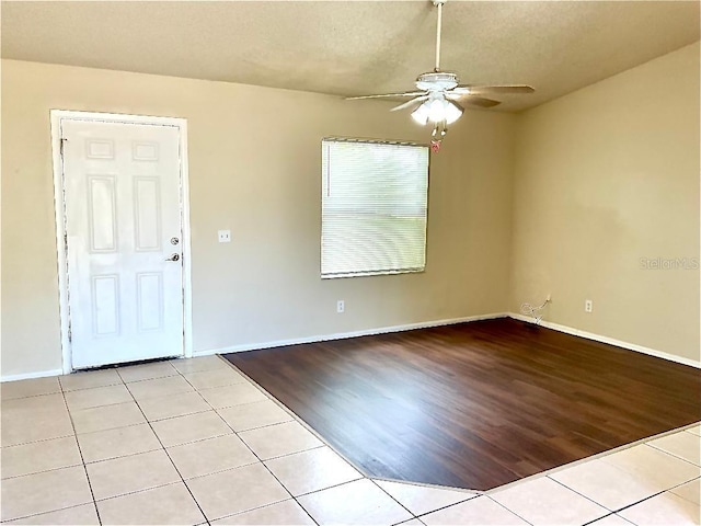 empty room with a textured ceiling, baseboards, a ceiling fan, and light tile patterned floors