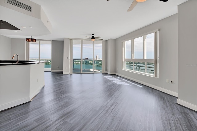 unfurnished living room featuring ceiling fan with notable chandelier, baseboards, and dark wood-style flooring