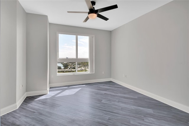 unfurnished room with dark wood finished floors, a ceiling fan, and baseboards