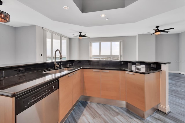 kitchen featuring light wood finished floors, open floor plan, dark stone countertops, stainless steel dishwasher, and a sink