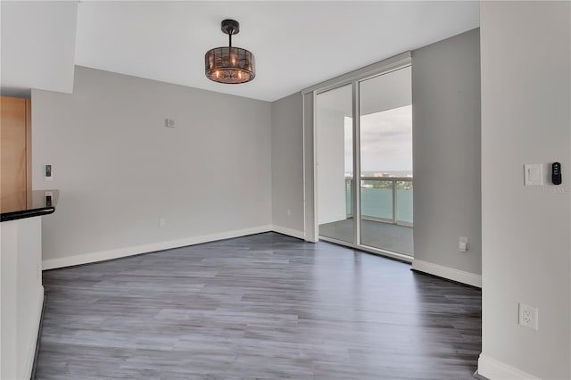 empty room featuring a wall of windows, baseboards, and wood finished floors