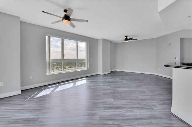 unfurnished living room featuring wood finished floors, a ceiling fan, and baseboards