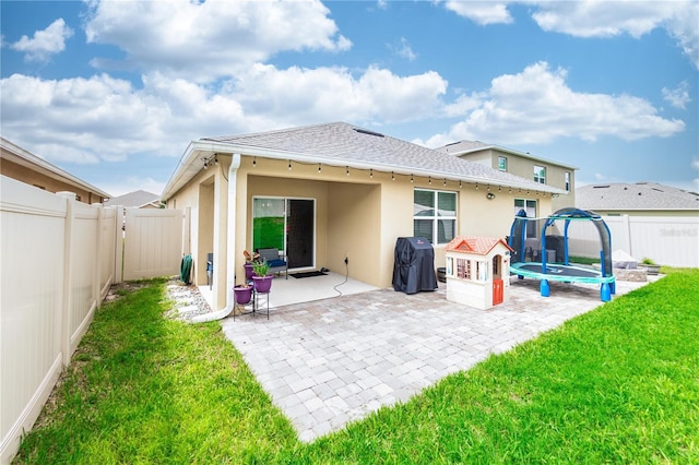 rear view of house with a fenced backyard, stucco siding, a trampoline, a patio area, and a lawn