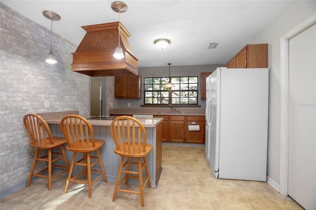 kitchen with visible vents, brick wall, a peninsula, freestanding refrigerator, and a sink