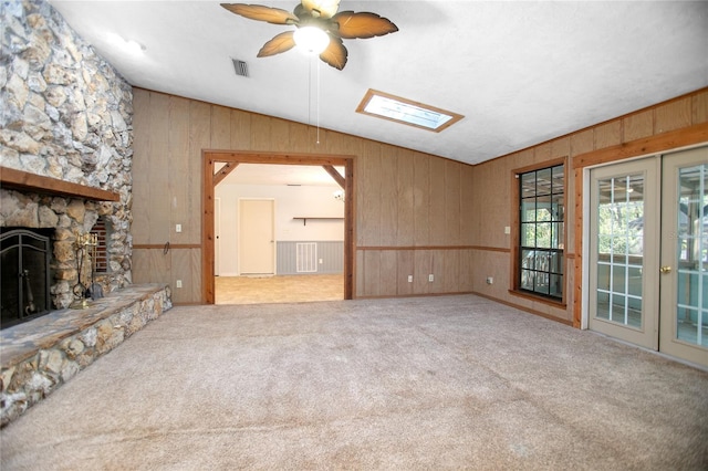 unfurnished living room featuring vaulted ceiling with skylight, visible vents, carpet flooring, and a stone fireplace